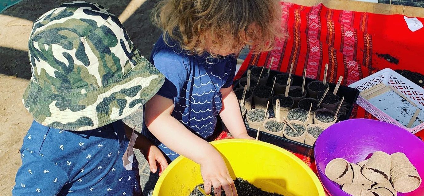 Preschool children in sunhats playing with sand and buckets outdoors
