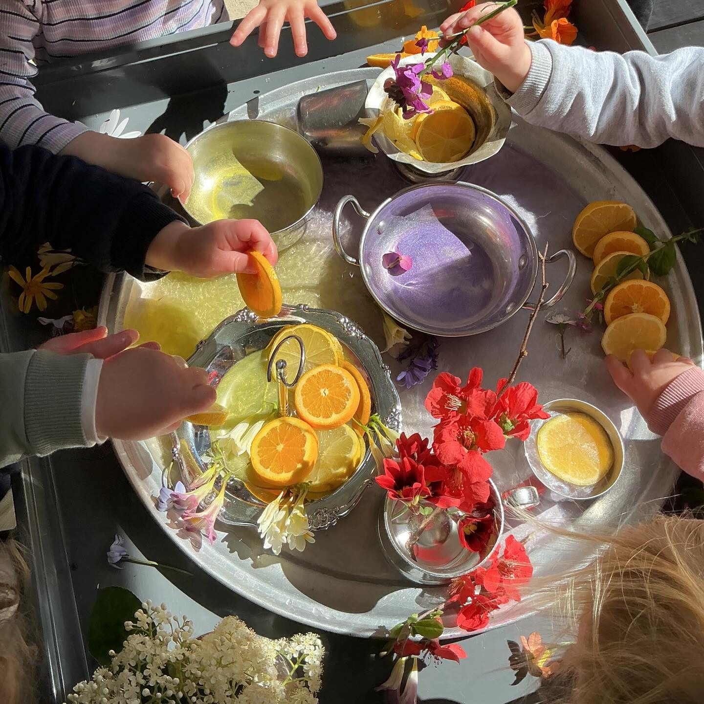 Children exploring a sensory tray of citrus, flowers and water